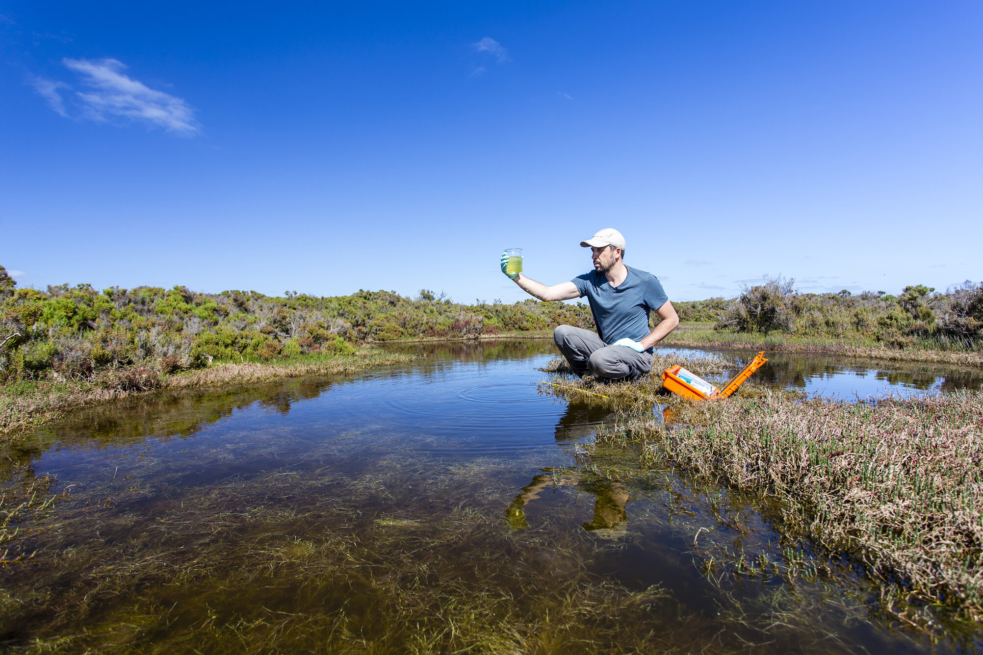 A man holding up a water sample near a river