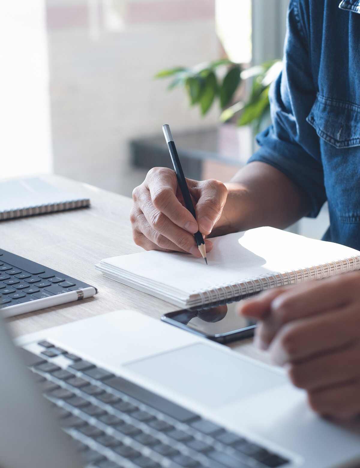 Closeup of a person writing in his notebook while also on his computer