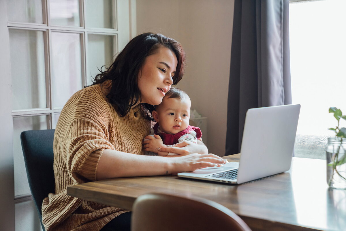 A student holding a baby while looking at her computer